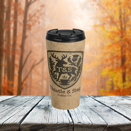 Kraft paper design on travel coffee cup with Thistle & Stag Coffee Co. logo and black lid on a wooden surface with autumn trees in the background